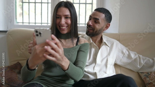 Fototapeta Excited girlfriend showing positive news on cellphone device to boyfriend. Happy couple celebrating successful notification message while holding phone