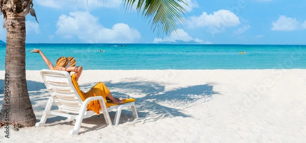 Fototapeta Happy Asian traveler woman relaxing on beach chair at tropical sandy beach with palm tree and beautiful blue sky. Summer vacation concept. Copy space.