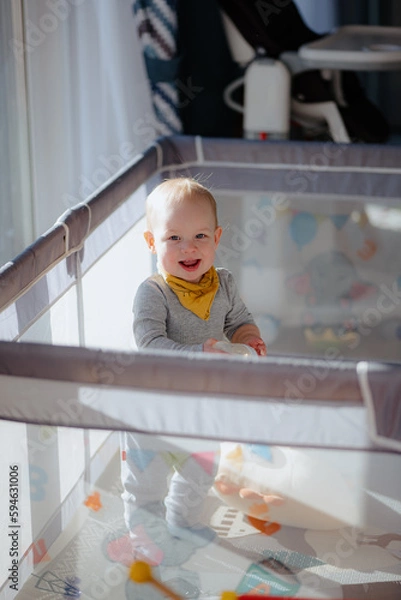Obraz Cute laughing baby boy toddler playing in playpen, Adorable child having fun indoor, Portrait of little smiling kid standing in crib, Small toddler in playpen