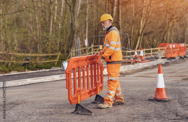 Fototapeta Builder placing safety barriers and red traffic cones during roadworks