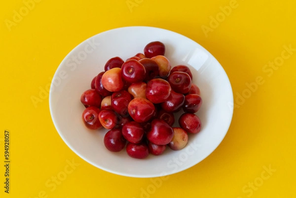 Fototapeta Fresh ripe cherries in a white plate on a yellow background. Close-up. Healthy food. Vegetarian breakfast.