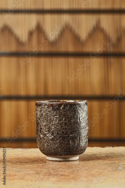 Fototapeta Ceramic striped cup on wooden table in bamboo screen (Still life