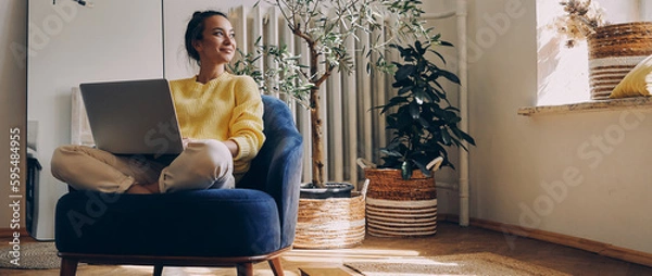 Obraz Attractive young woman using laptop while relaxing in a comfortable chair at home