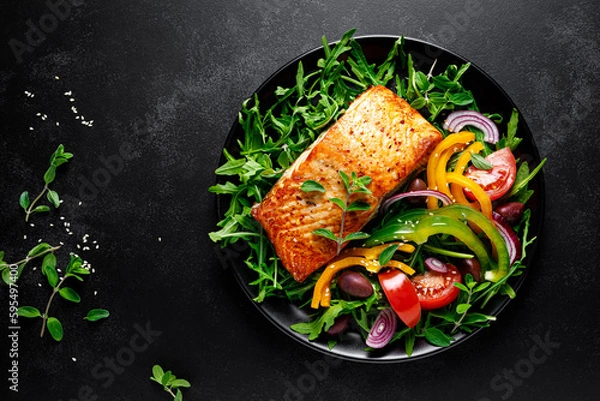 Obraz Salmon fillet grilled and fresh vegetable green salad of arugula with tomatoes, olives and bell pepper on black background, healthy food, mediterranean diet, top view