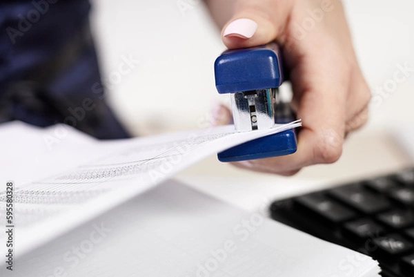 Obraz Office worker staples documents at office desk
