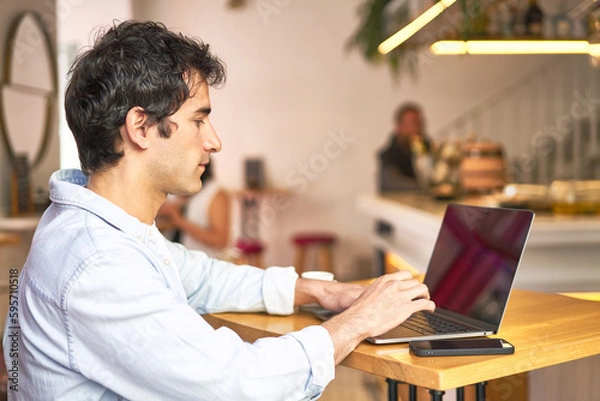 Fototapeta Caucasian millennial happily browsing on laptop at cozy cafe.