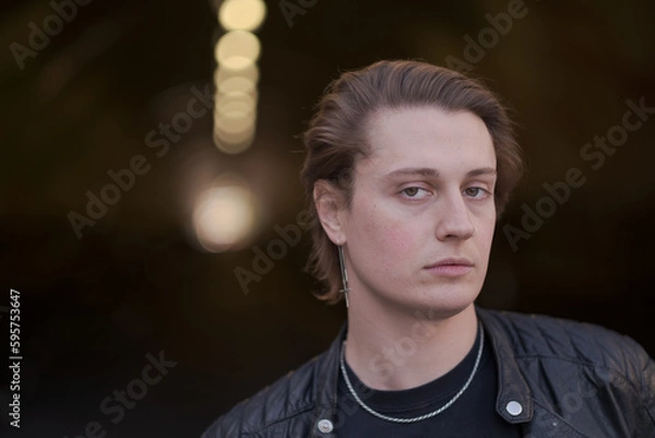 Fototapeta A genderfluid (LGBTQ) model poses outside, in front of a tunnel, to express calmness and a sense of overcoming challenges. Their hair is combed back, and they are wearing a black leather jacket.