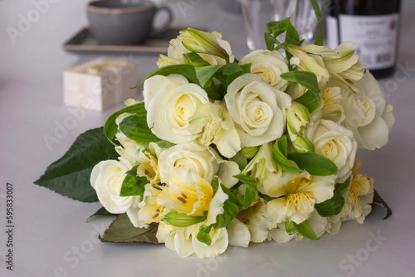 Obraz A festive tender bouquet with light roses on the table on a bottle of wine and a gift box