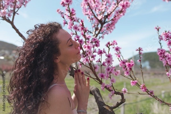 Obraz A young girl among beautiful peach flowers in full bloom. Pink peach blossom garden. Springtime.