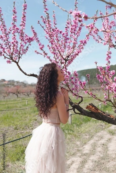 Obraz A young girl among beautiful peach flowers in full bloom. Pink peach blossom garden. Springtime.