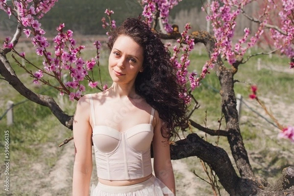 Obraz A young girl among beautiful peach flowers in full bloom. Pink peach blossom garden. Springtime.