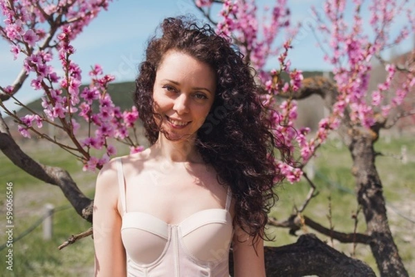 Obraz A young girl among beautiful peach flowers in full bloom. Pink peach blossom garden. Springtime.