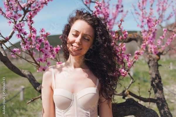 Obraz A young girl among beautiful peach flowers in full bloom. Pink peach blossom garden. Springtime.