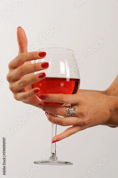 Obraz Woman's hands with red manicure holding glass of red wine on white background