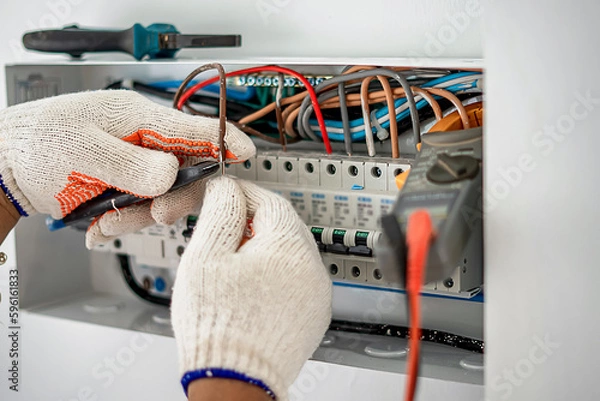 Fototapeta An electrical engineer is working on a home electrical control panel system and checking the current with a voltmeter.