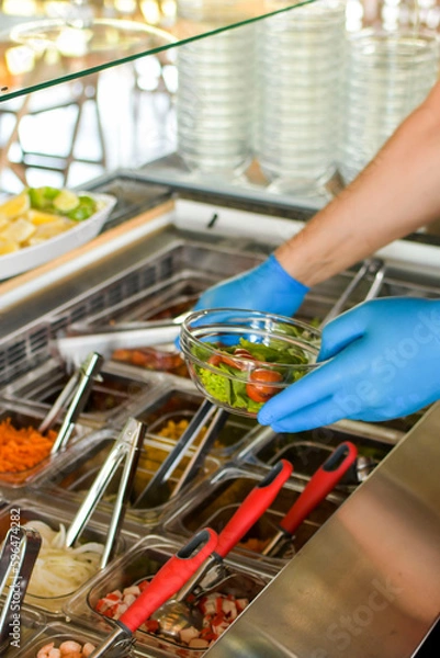 Fototapeta 
Arms of man with blue gloves, serving poke salad in a bowl