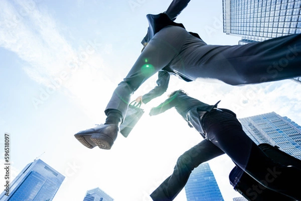 Obraz 大都会で青空に向かって2人のチームで飛翔しジャンプするダイナミックで勢いのあるビジネスマンの男性