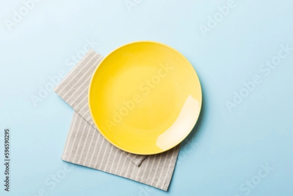 Obraz Top view on colored background empty round yellow plate on tablecloth for food. Empty dish on napkin with space for your design