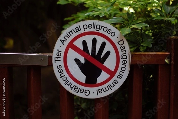 Fototapeta A round sign on a wooden fence informing about dangerous animals