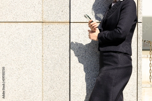 Obraz 屋外で立ち止まってスマホを操作しているビジネスウーマン	