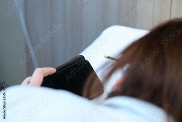 Obraz ベッドで寝ながらスマホを見ている女性