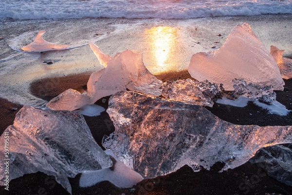 Fototapeta Pure Ice Shining on Black Volcanic Sand at Sunset. Icebergs from Glacier in Sun Rays. Clear Ice in Ocean Waves. Famous Tourist Location in North Europe Country. Travel Destination Diamond Beach..
