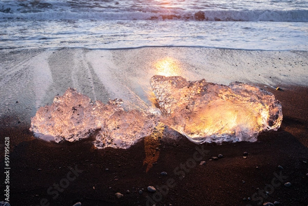 Fototapeta Pure Ice Shining on Black Volcanic Sand at Sunset. Icebergs from Glacier in Sun Rays. Clear Ice in Ocean Waves. Famous Tourist Location in North Europe Country. Travel Destination Diamond Beach..