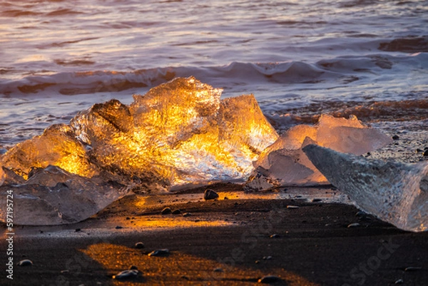 Fototapeta Pure Ice Shining on Black Volcanic Sand at Sunset. Icebergs from Glacier in Sun Rays. Clear Ice in Ocean Waves. Famous Tourist Location in North Europe Country. Travel Destination Diamond Beach..