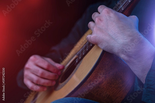 Fototapeta The guy in the dark shirt is plucking the strings of a six-string guitar