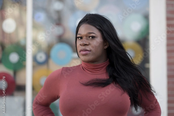 Fototapeta Wearing a sleek, long-sleeved turtleneck, a model expresses a colorful, confident pose. As a Black woman of trans experience, she affirms her freedom to be her authentic self.