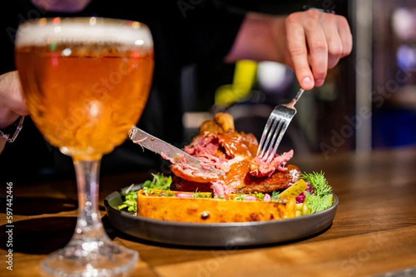 Fototapeta man cuts a pork knuckle with a knife and fork