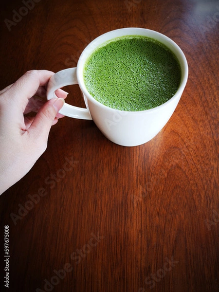 Obraz Hand holding a cup of green tea with milk or hot matcha latte on the wooden table in cafe with copy space    
