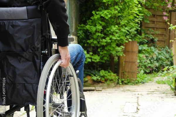 Fototapeta A disabled person in a wheelchair. A man with reduced mobility in an alley with vegetation.