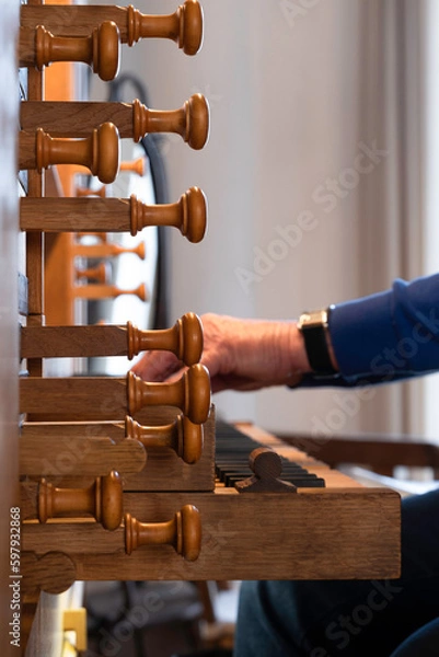 Fototapeta Organist playing a church organ. Seen from the side, narrow depth of field, focus on the wooden organ stops