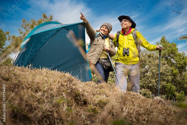 Obraz Senior couple of hikers spending a day on a mountain while woman is aiming at distance.