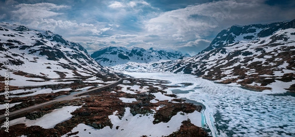 Fototapeta Snowy landscape of Hardangervidda national park with mountains and a road along icy lakes in Norway, from above