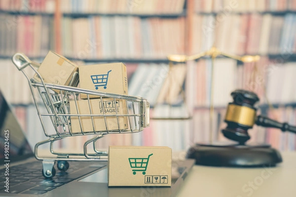 Fototapeta Consumer rights and consumer protection, business law concept : Shopping basket, shopping boxes and a shopping cart on a laptop computer with judge gavel, balance sale of justice and bookshelf behind.