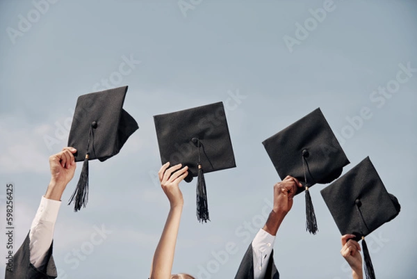 Obraz Close-up of many hands holding mortarboards against blue sky after graduation ceremony