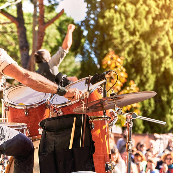 Fototapeta Summer music festival at the park. Music band playing on the stage. The drummer plays while the singer raises his fist in a successful pose