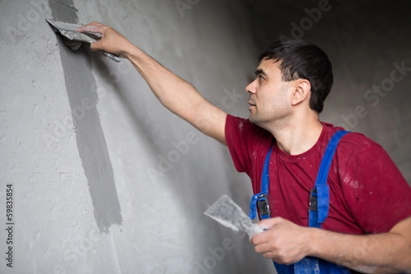 Fototapeta worker with spatula makes repairs smears on wall putty