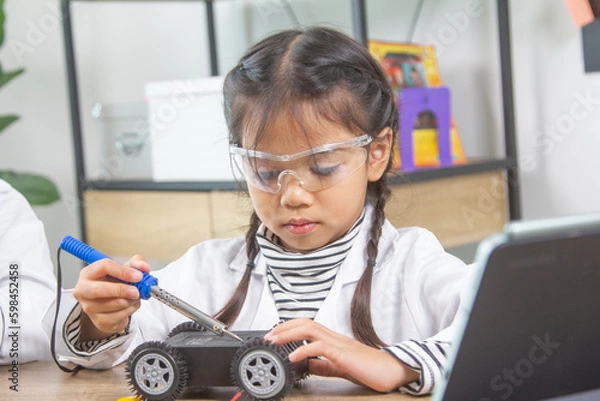 Obraz School student making robotic cars. Girl at robotics school makes robot managed from the constructor, child learns robot constructing.