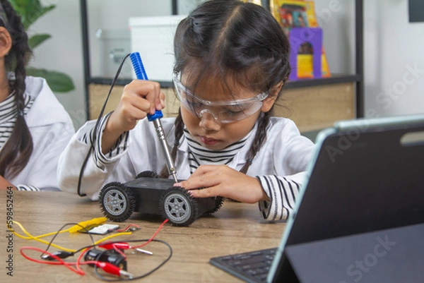 Fototapeta School student making robotic cars. Girl at robotics school makes robot managed from the constructor, child learns robot constructing.