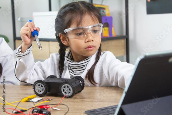 Fototapeta School student making robotic cars. Girl at robotics school makes robot managed from the constructor, child learns robot constructing.