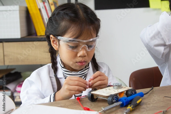 Fototapeta School student making robotic cars. Girl at robotics school makes robot managed from the constructor, child learns robot constructing.