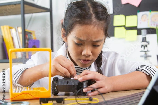 Fototapeta School student making robotic cars. Girl at robotics school makes robot managed from the constructor, child learns robot constructing.