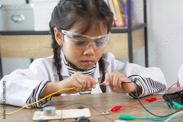 Obraz School student making robotic cars. Girl at robotics school makes robot managed from the constructor, child learns robot constructing.