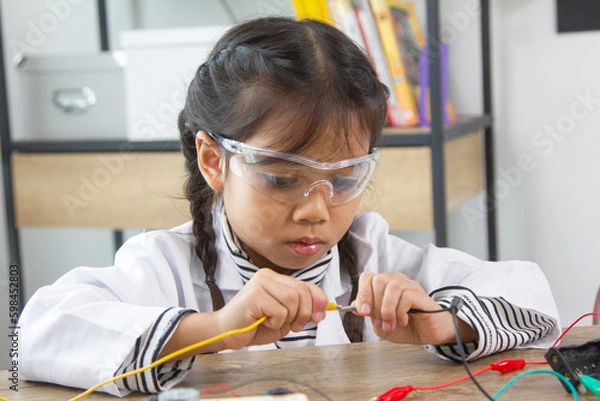 Fototapeta School student making robotic cars. Girl at robotics school makes robot managed from the constructor, child learns robot constructing.