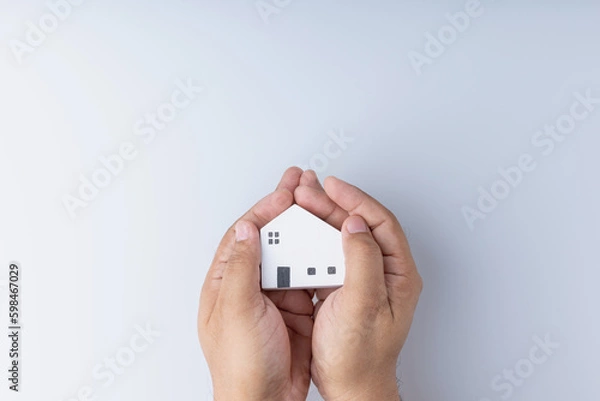 Fototapeta Real estate investing concepts, finance, banking, and saving money. A little wooden house model in hand, white background with copy space. Business of residence can make a profit in the future.