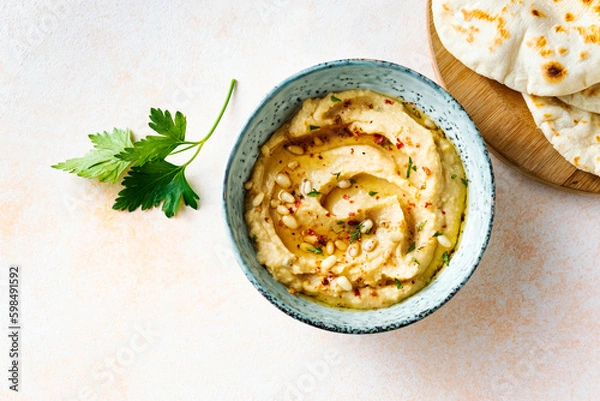 Fototapeta Homemade hummus with pine nuts and pita on a beige background, top view.