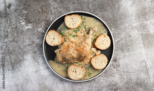 Fototapeta Stewed chicken leg with garlic and bread  on a round plate on a dark grey background. Top view, flat lay
